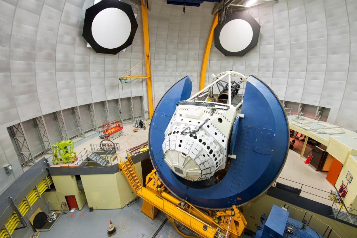 A telescope and camera system sit inside an observatory dome.