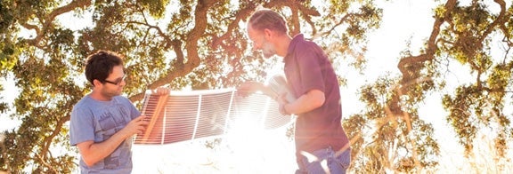 PHOTO: Two SLAC researchers holding thin-film photovoltaic material in front of wash of sunlight.