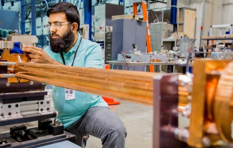 Image - Muhammad Shumail, a PhD student, inspects the microwave undulator that he worked to design and build. (Fabricio Sousa/SLAC)