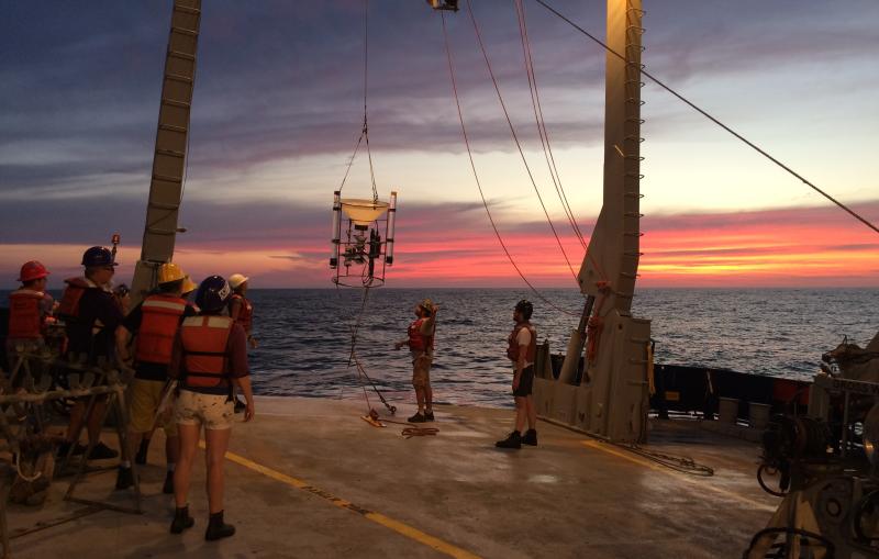 Scientists watch from a ship deck as a sample is hauled in from the ocean.