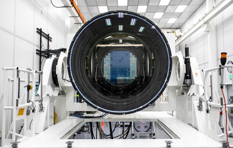 A digital sensor array is visible through a large camera lens inside a white room.