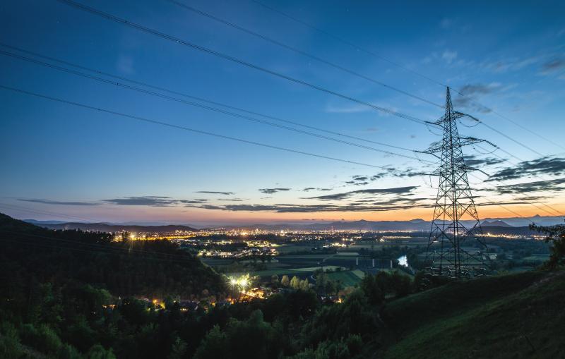View of a city at twilight with a power transmission tower in foreground 