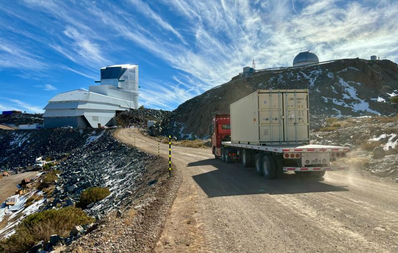 A semi truck traveling a gravel road approaches two large telescope facilities.