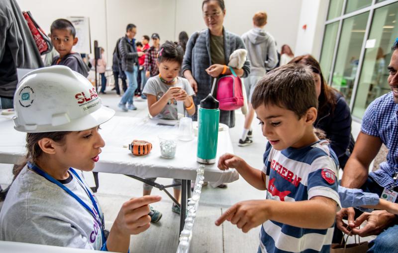 Scientist wearing a hard had showing a young person how to do a science experiment. 