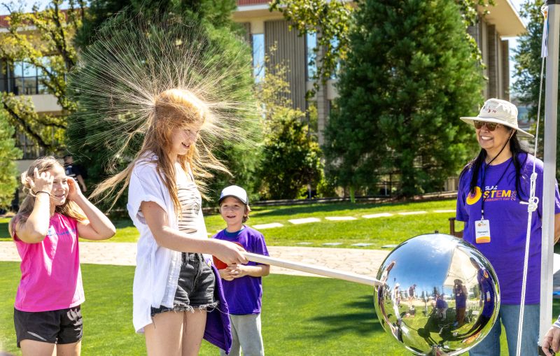 A girl experiences static electricity from a Van de Graaff generator at a outdoor SLAC STEM Community Day event, making her hair stand on end.
