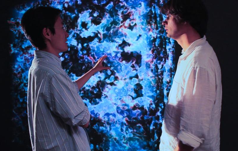  Ji-hoon Kim (left) and Ralf Kaehler (right), both of KIPAC, stand before a snapshot of a large-scale reionization simulation. The blue regions indicate hot, ionized hydrogen gas. Photo by Brad Plummer.