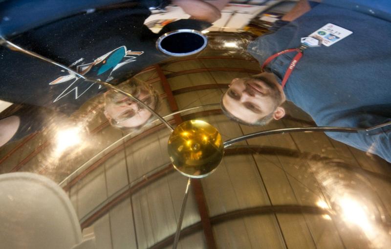 Team members Howard Rogers (left) and Peter Lewis (right) are reflected in the gold-coated hemispherical mirror of RASICAM – the Radiometric All Sky Infrared Camera. 