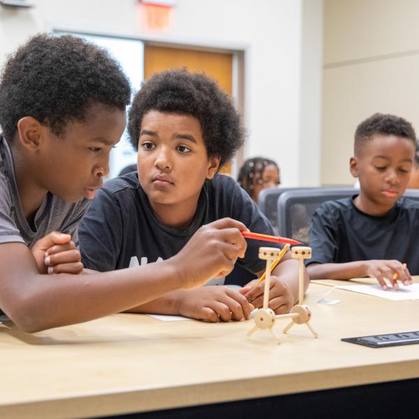 Two students build a small structure in a classroom. 