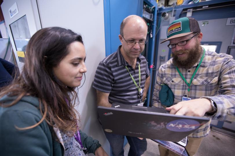 SSRL scientist Sam Webb at a beam line with two visiting scientists looking at a laptop
