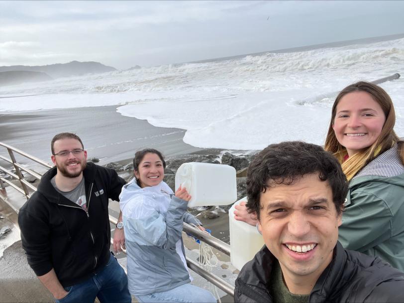 Los investigadores se paran cerca del Océano Pacífico sosteniendo baldes en los que recolectaron agua de mar para un experimento que convierte el agua de mar en combustible de hidrógeno.