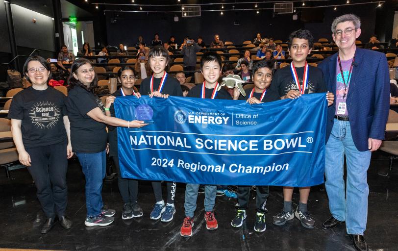 Middle schools students hold up a blue National Science Bowl banner with SLAC Director John Sarrao.