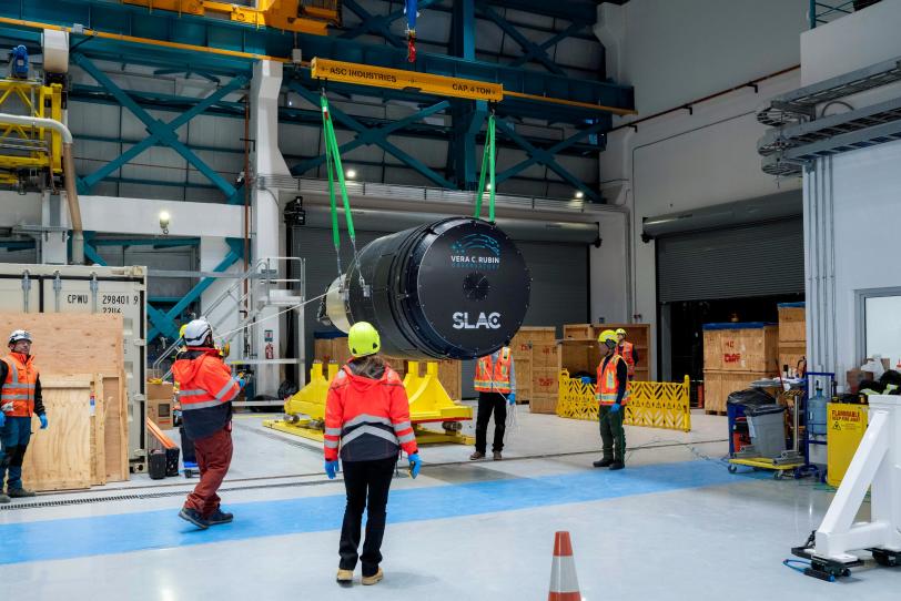 Researchers watch as a large cylindrical camera is lifted out of its crate.