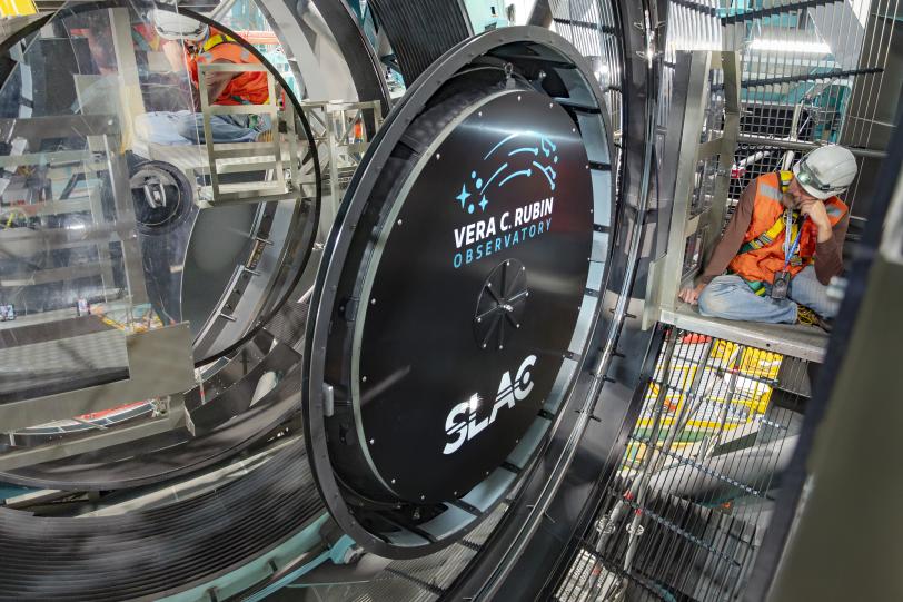 A person in a hard hat looks at a giant black lens cap surrounded by a mirror.