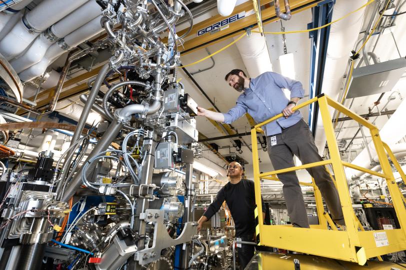 Two individuals in a lab maneuver around highly intricate machinery on a yellow platform.