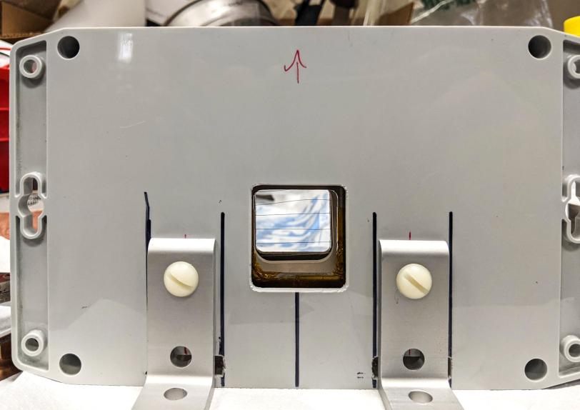 A detector prototype seen through a gray plastic protective enclosure with gold-plated tungsten wires at the center to measure the shape of an electron beam.