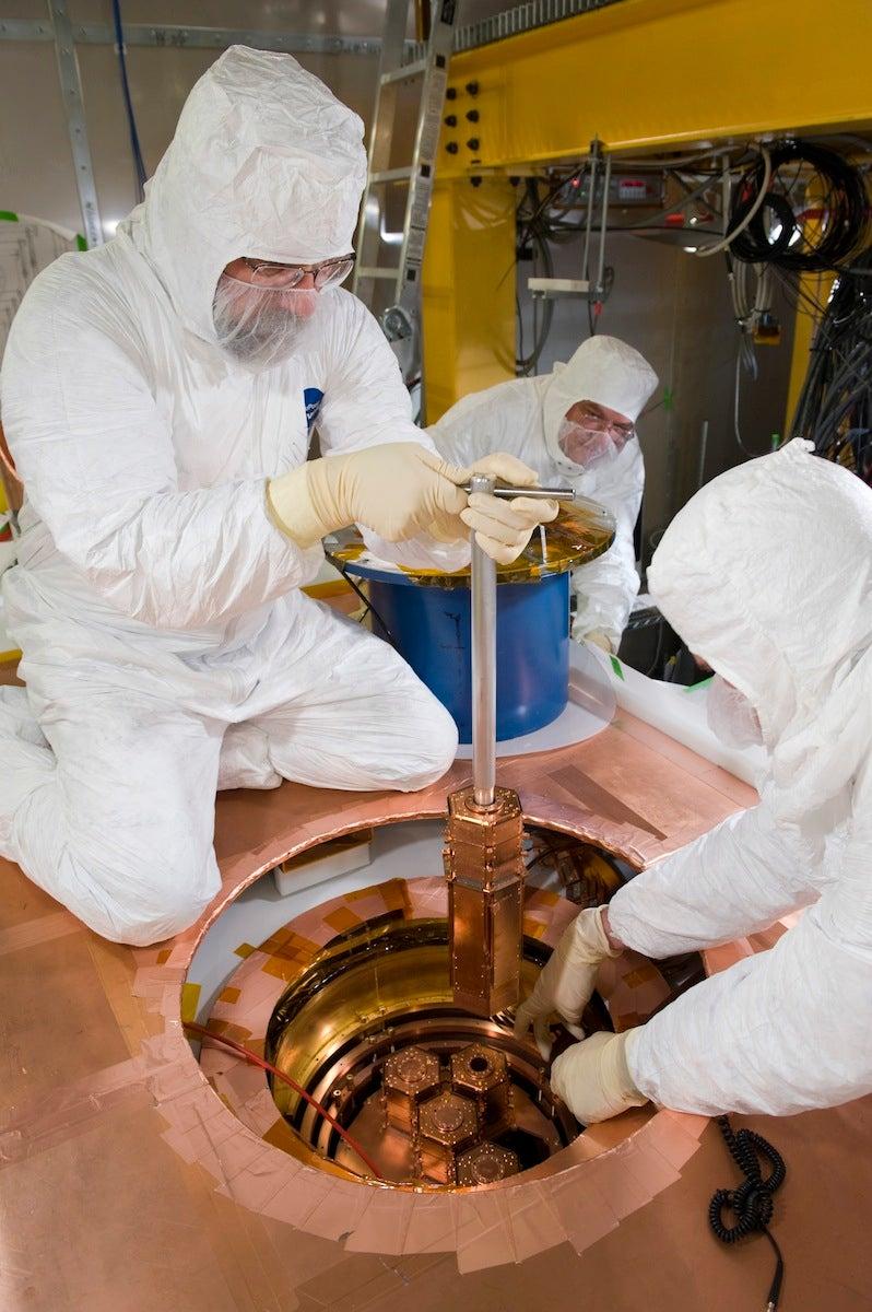 Photo of scientist in clean suit lifting dark matter detector from experiment