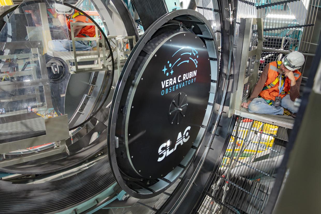 A person in a hard hat looks at a giant black lens cap surrounded by a mirror