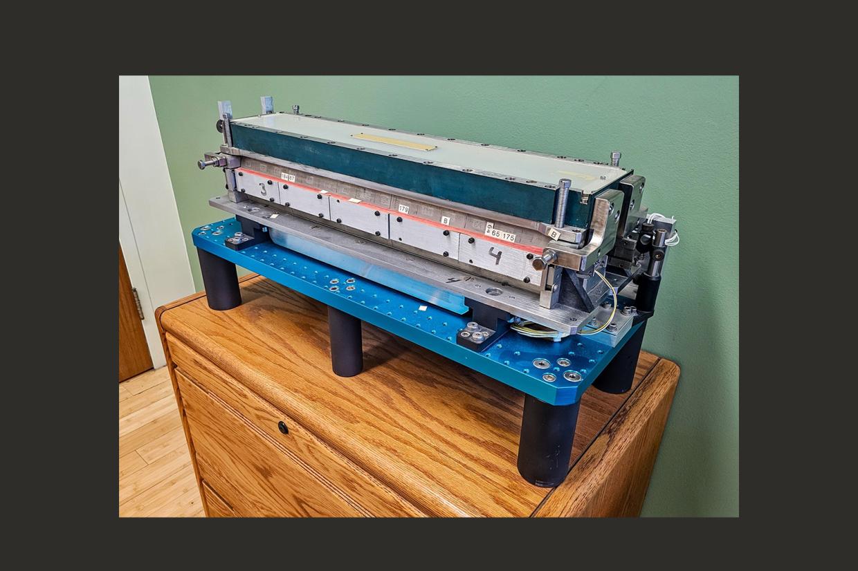 A blue and gray piece of lab equipment atop a wooden chest of drawers.