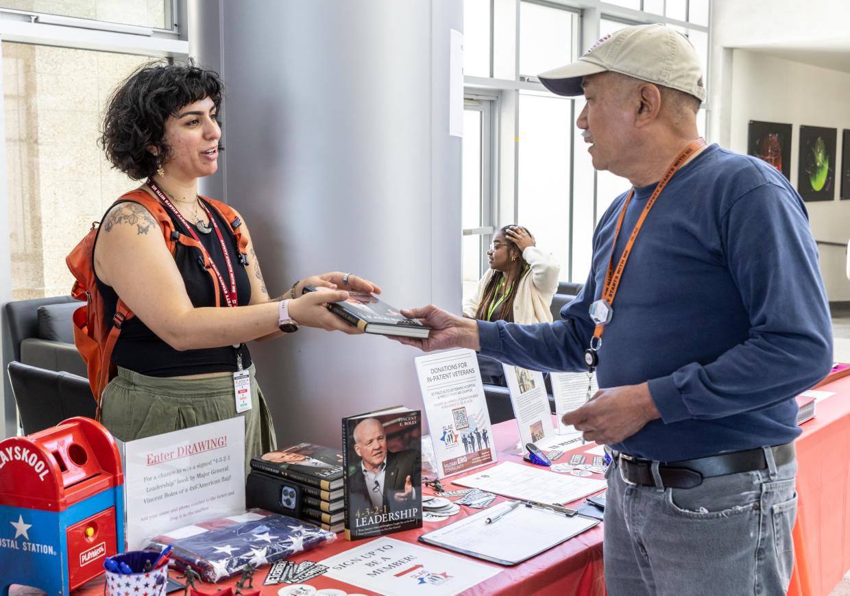 A person hands a book to a visitor while tabling at the event.