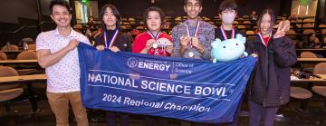 High school students hold up a blue National Science Bowl banner.