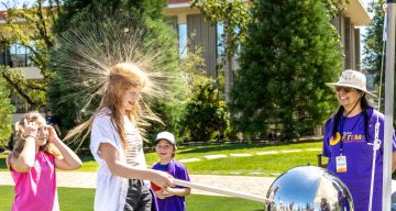 A girl experiences static electricity from a Van de Graaff generator at a outdoor SLAC STEM Community Day event, making her hair stand on end.