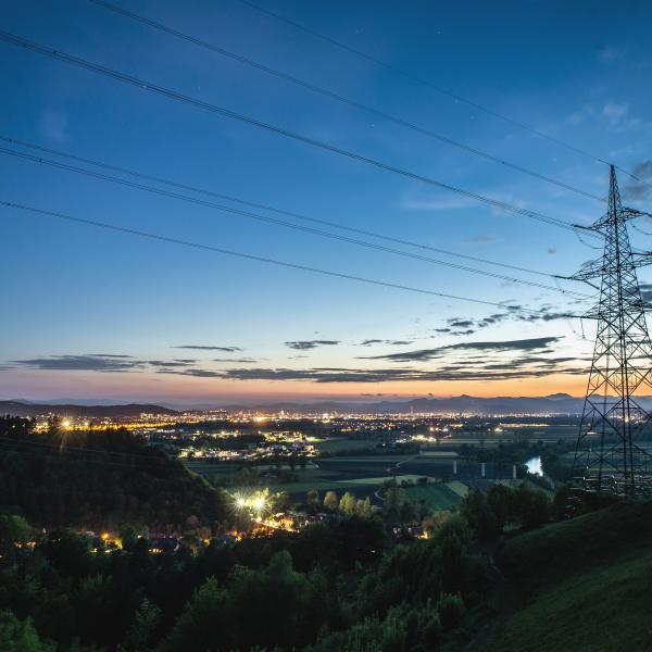View of a city at twilight with a power transmission tower in foreground 
