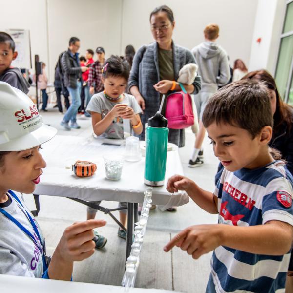 Scientist wearing a hard had showing a young person how to do a science experiment. 