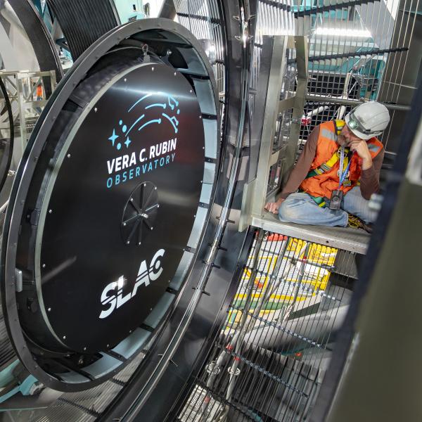 A person in a hard hat looks at a giant black lens cap surrounded by a mirror.