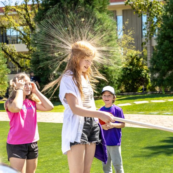 A girl experiences static electricity from a Van de Graaff generator at a outdoor SLAC STEM Community Day event, making her hair stand on end.