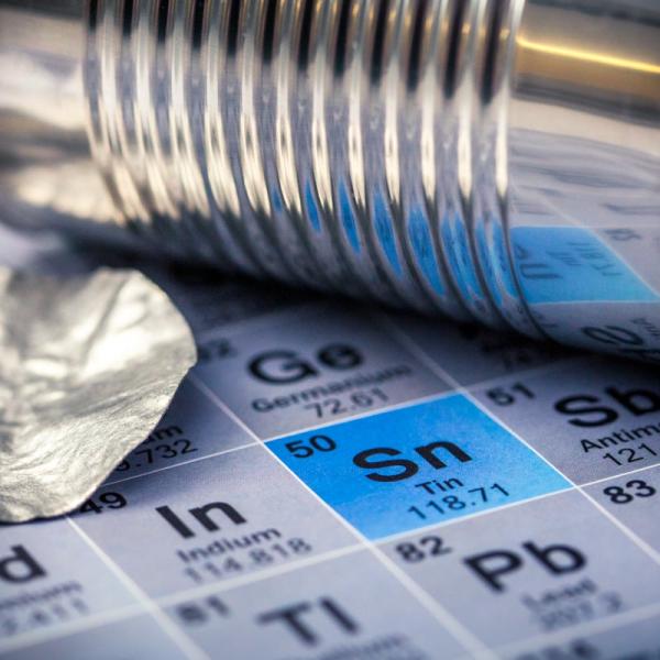 Photo - tin can and piece of scrap tin sitting on a periodic table of elements with tin "Sn" highlighted