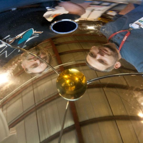 Team members Howard Rogers (left) and Peter Lewis (right) are reflected in the gold-coated hemispherical mirror of RASICAM – the Radiometric All Sky Infrared Camera. 