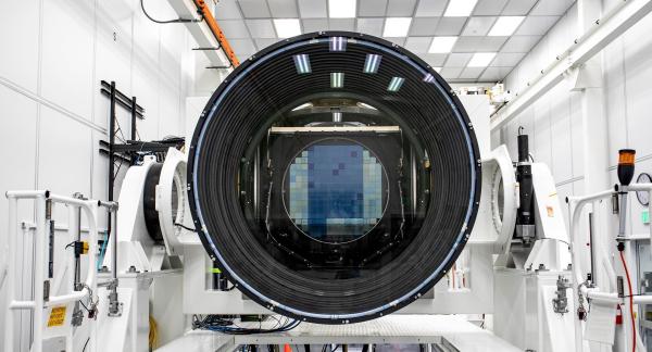 A digital camera sensor is visible through a large camera lens sitting inside a white room.