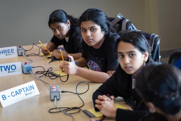 three middle school students sit at a table, holding buzzers for the competition in their hands, listening intently as questions are read