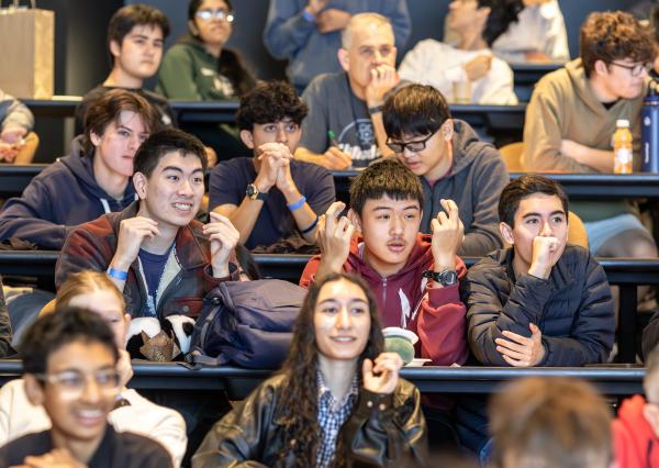 in a crowd of students, three students are in focus, and all three are focused on the activity they are watching (out of frame), looking very excited and engaged 